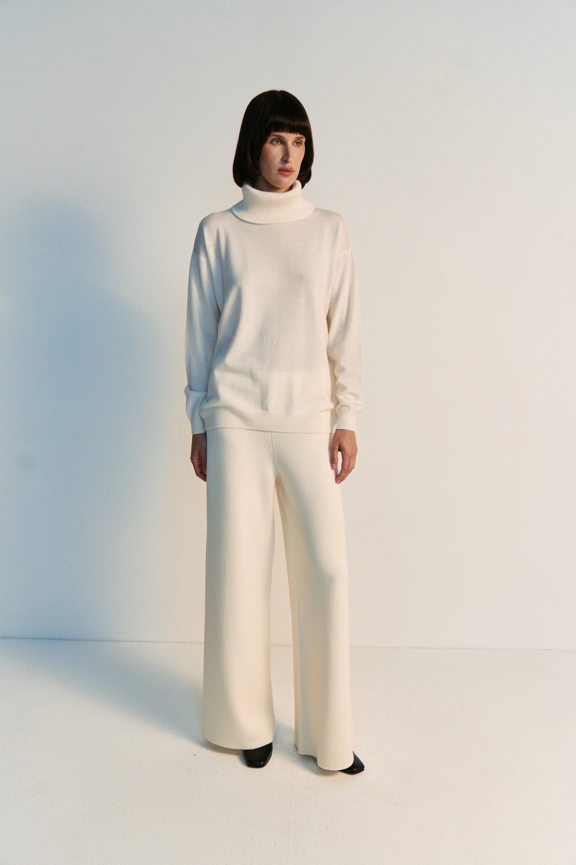 Person wearing a white outfit with wide-leg pants on a plain background