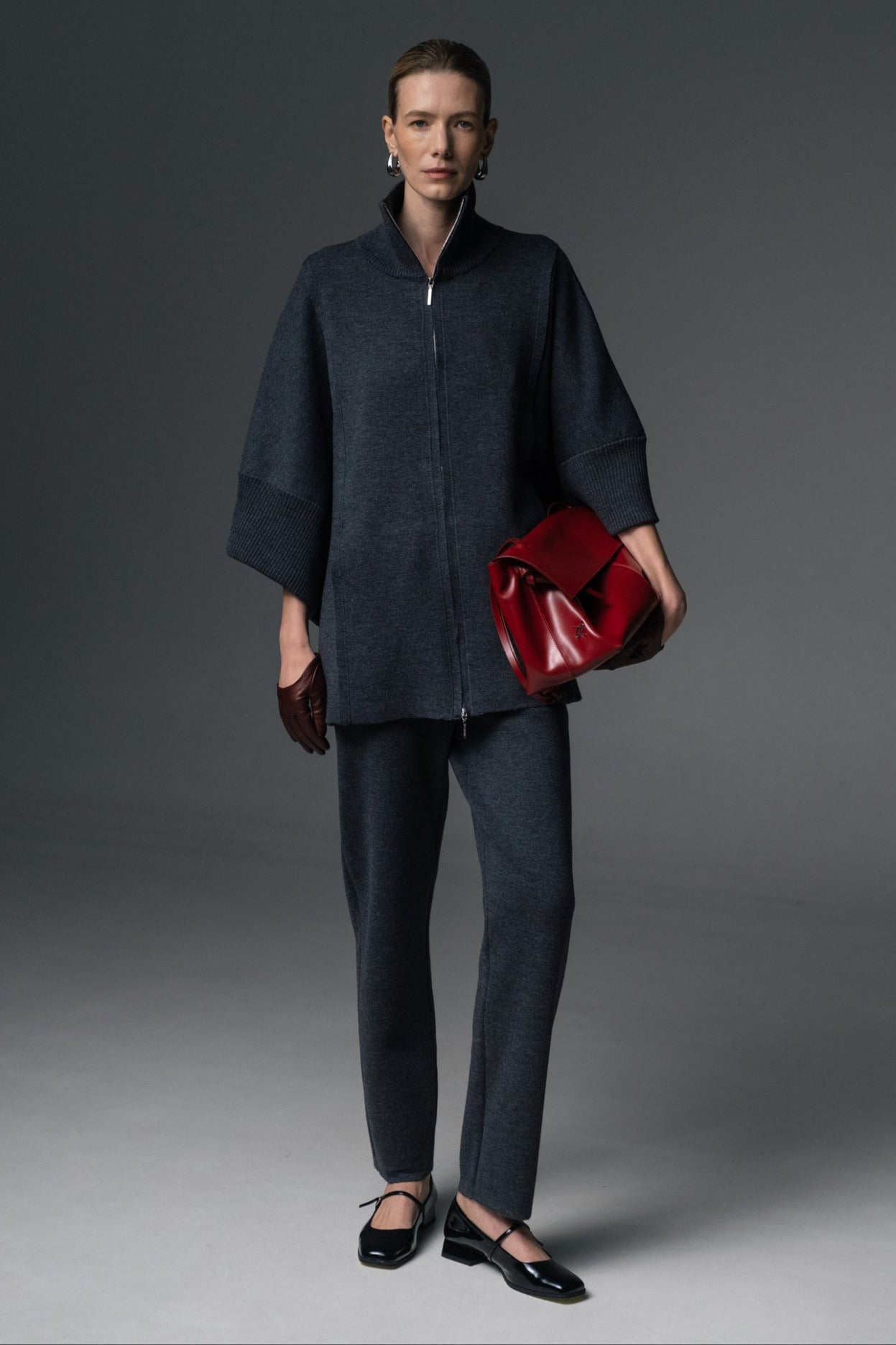 Person wearing a dark coat and pants with a red bag on a gray background