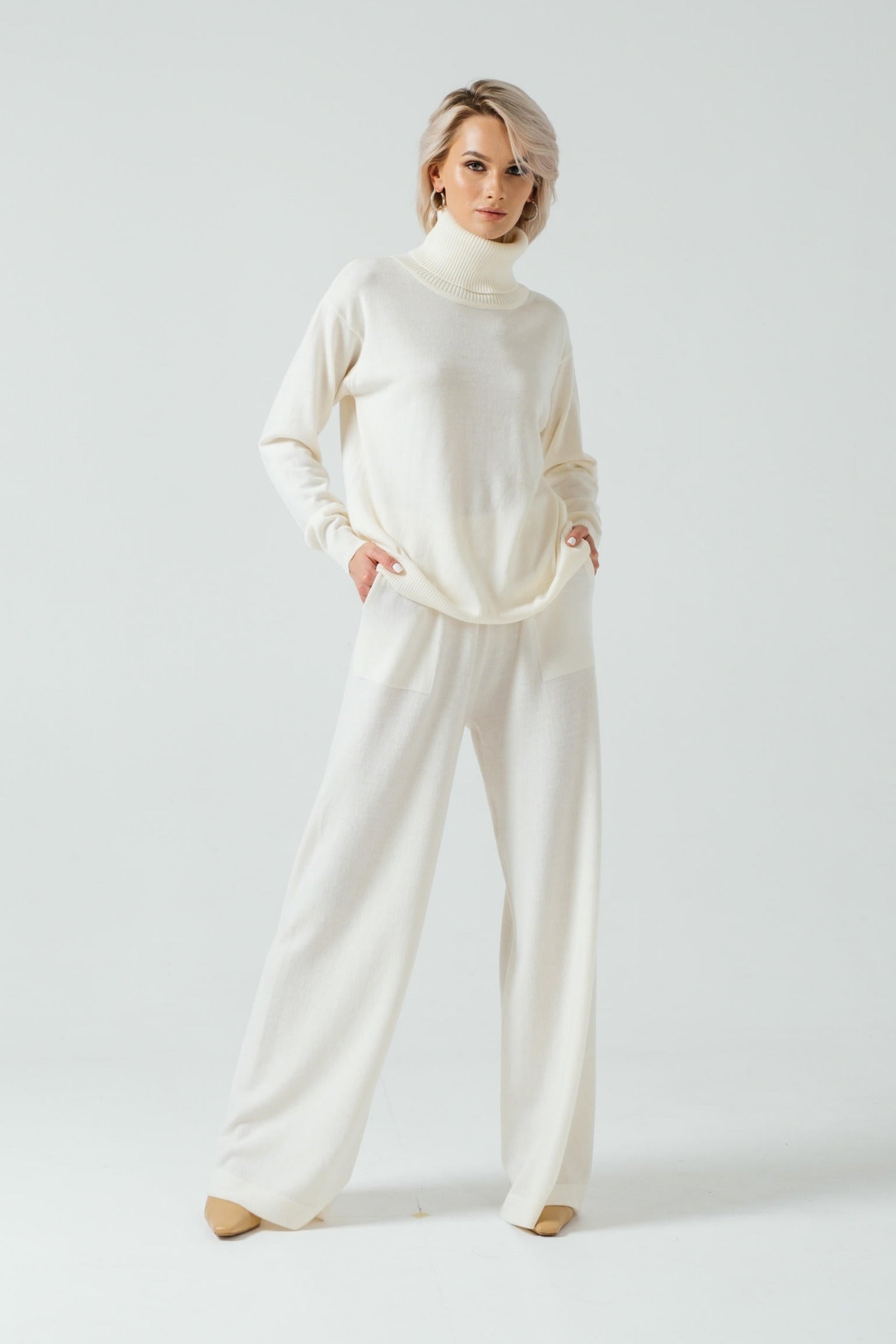 Woman wearing a white turtleneck sweater and pants on a light gray background