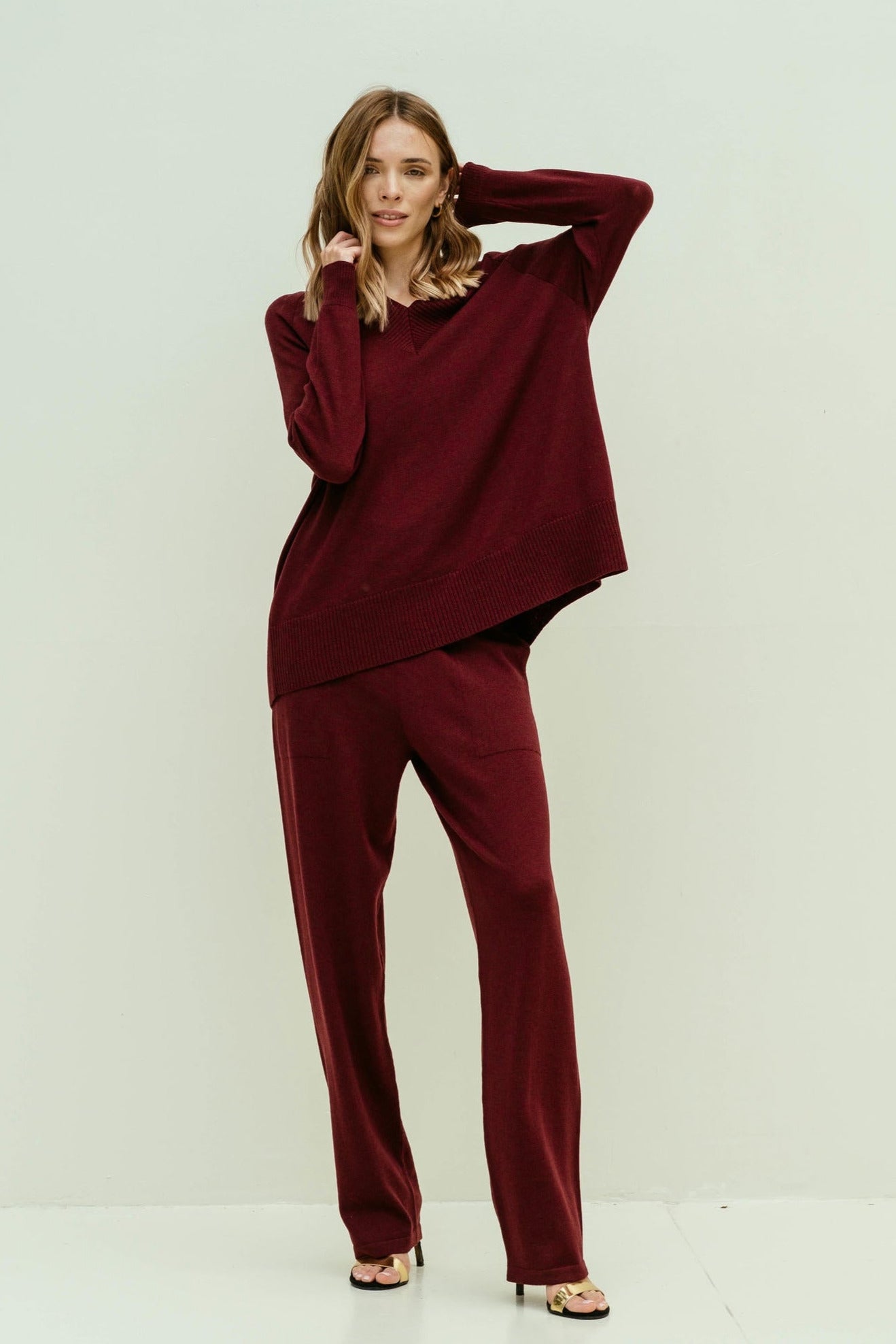Model wearing wine-colored merino wool V-neck jumper and matching pants, styled as a relaxed two-piece demi-season outfit from Viamaro