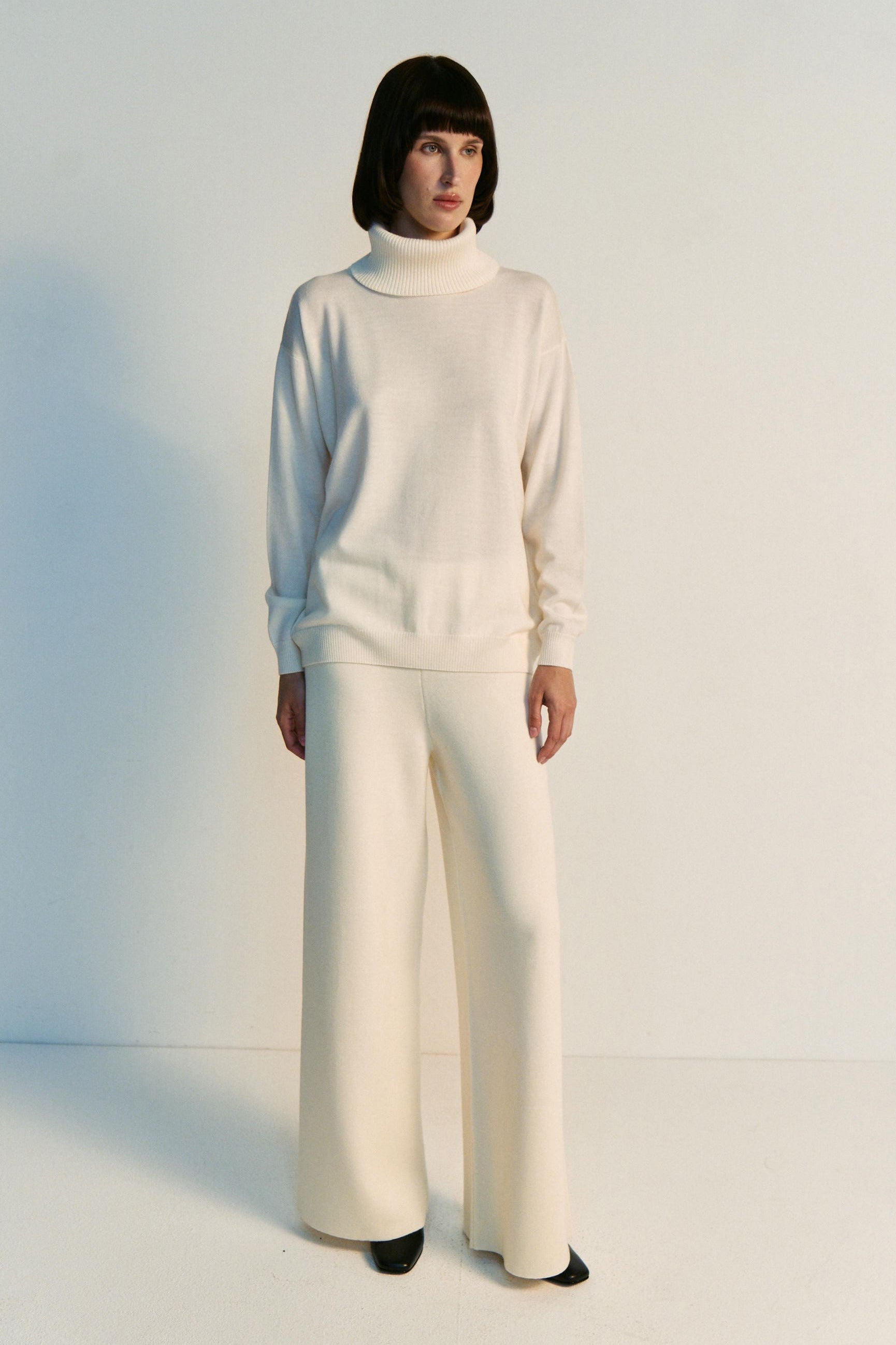 Person wearing a white outfit with wide-leg pants against a plain background