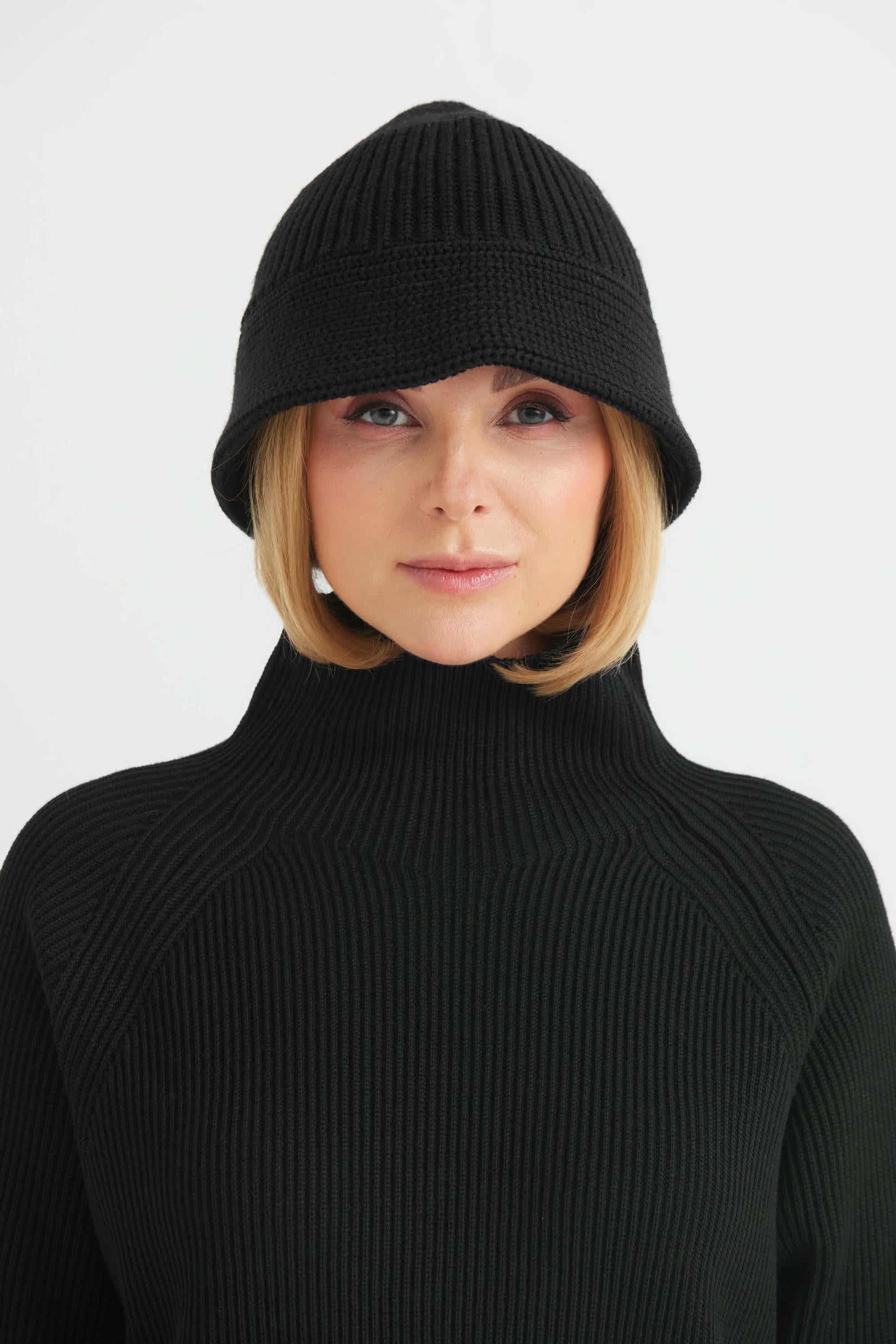 Woman wearing a black knit beanie and turtleneck sweater on a light gray background