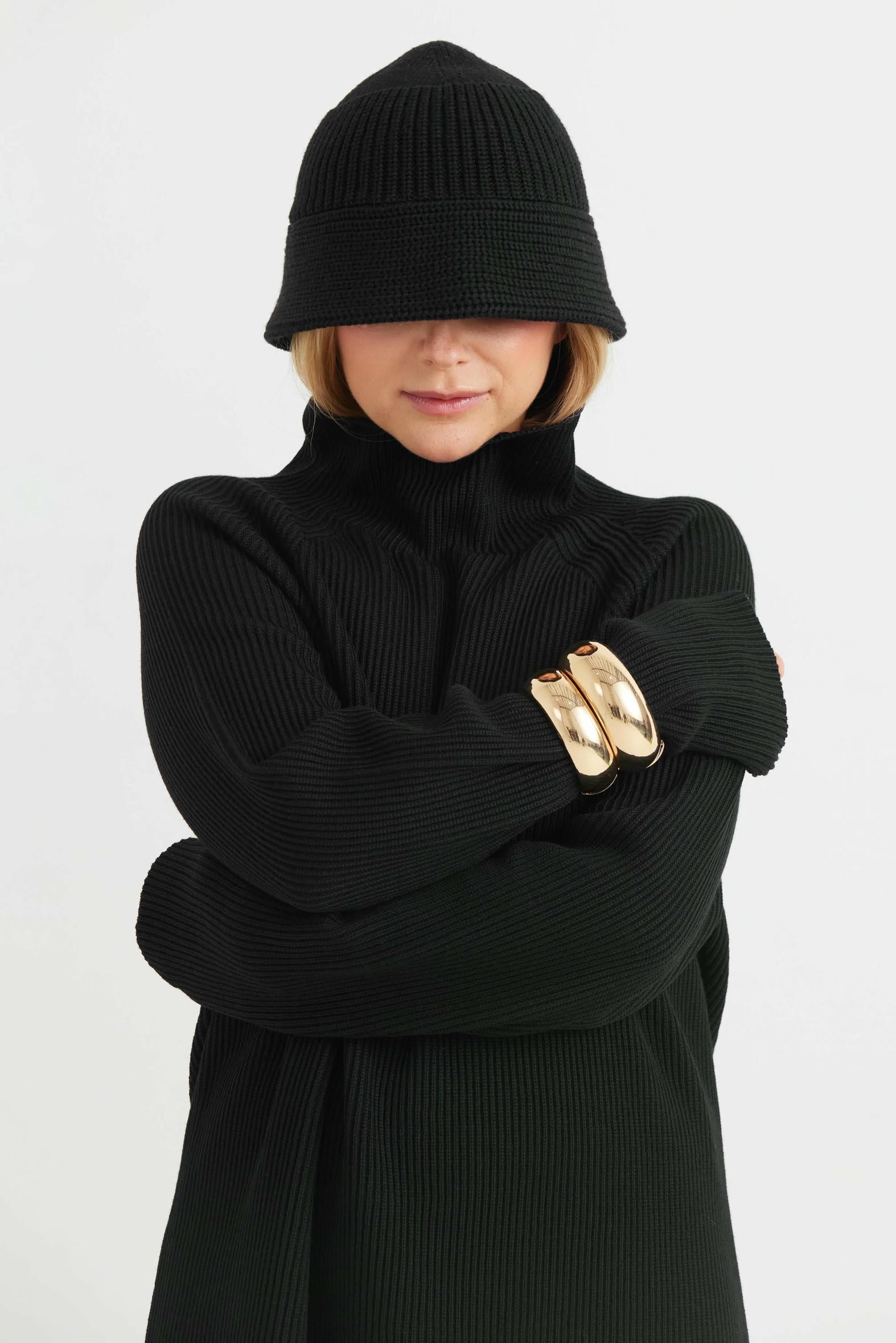 Person wearing a black knit outfit with a beanie on a white background