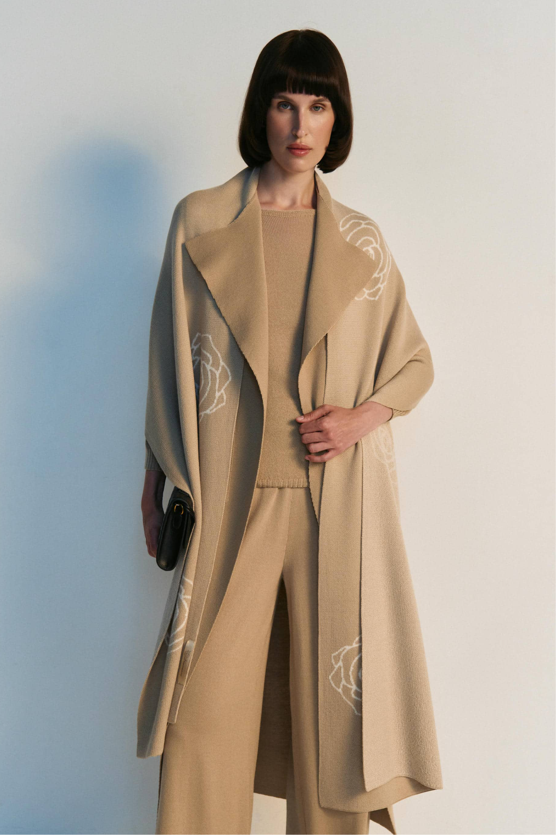 Woman wearing a beige coat with intricate designs against a white background