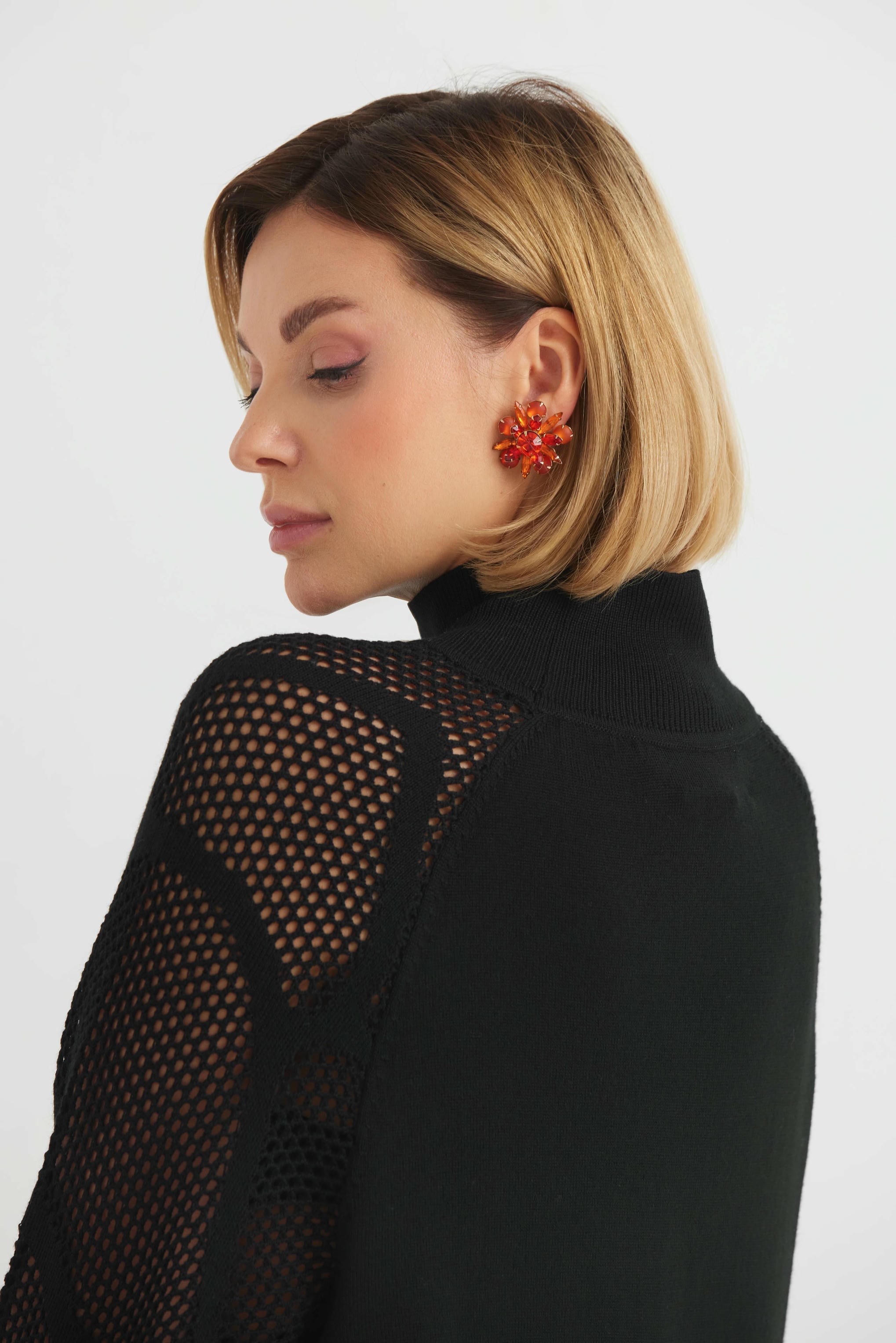 Woman wearing a black mesh back top with orange earrings on a white background