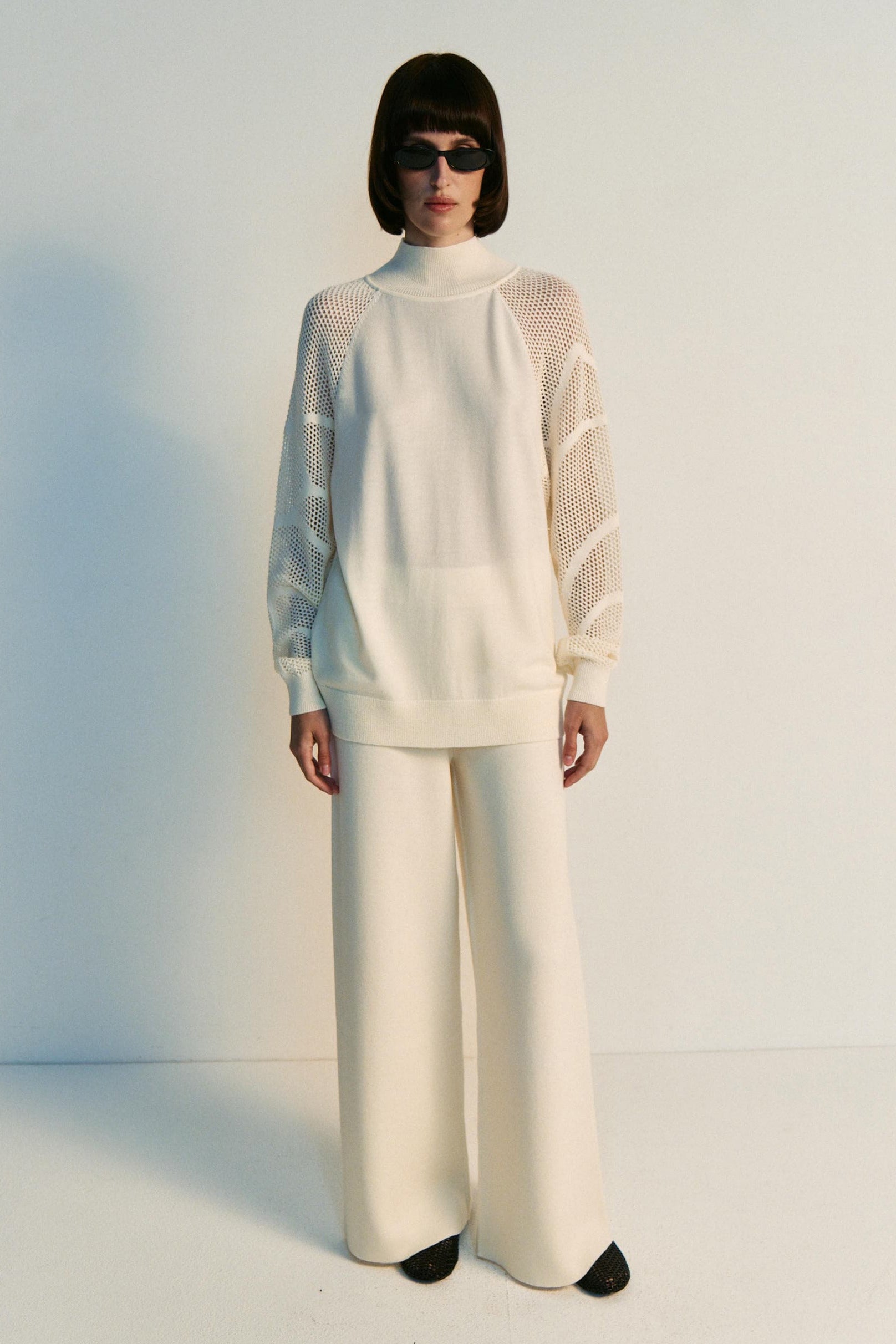 Person wearing a white outfit with sheer sleeves against a plain background