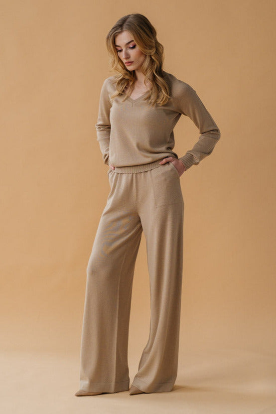 Woman wearing a beige sweater and pants against a beige background