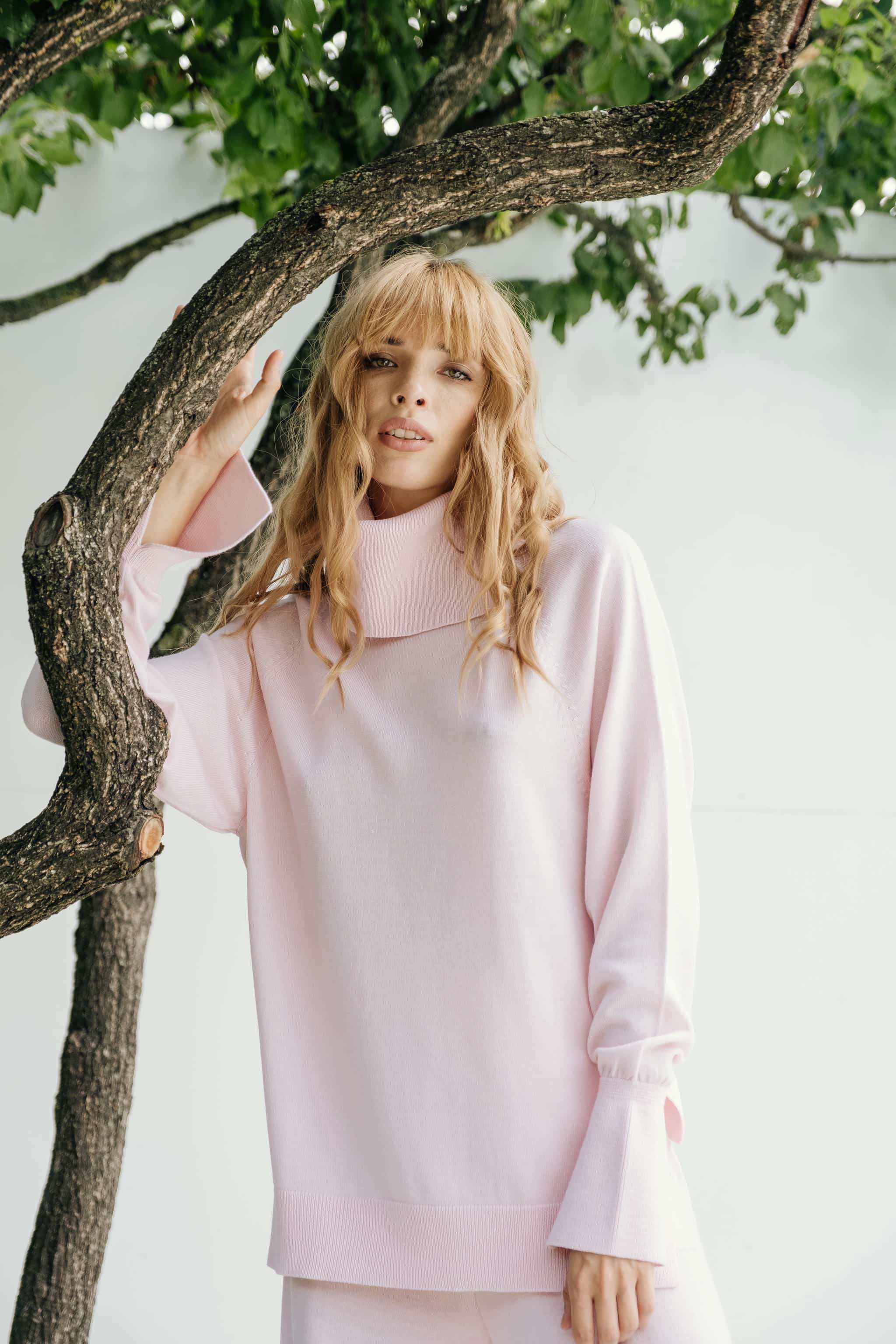 A woman standing outdoors wearing a pink turtleneck long-sleeved shirt.