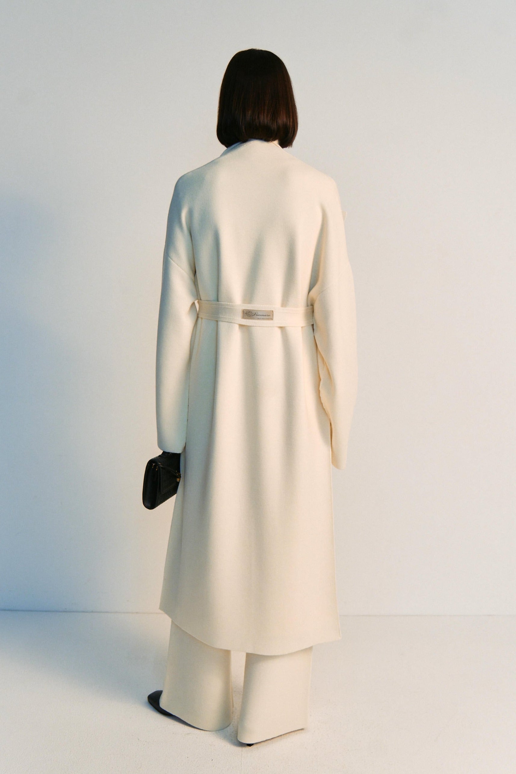 Person wearing a long cream coat standing against a white background
