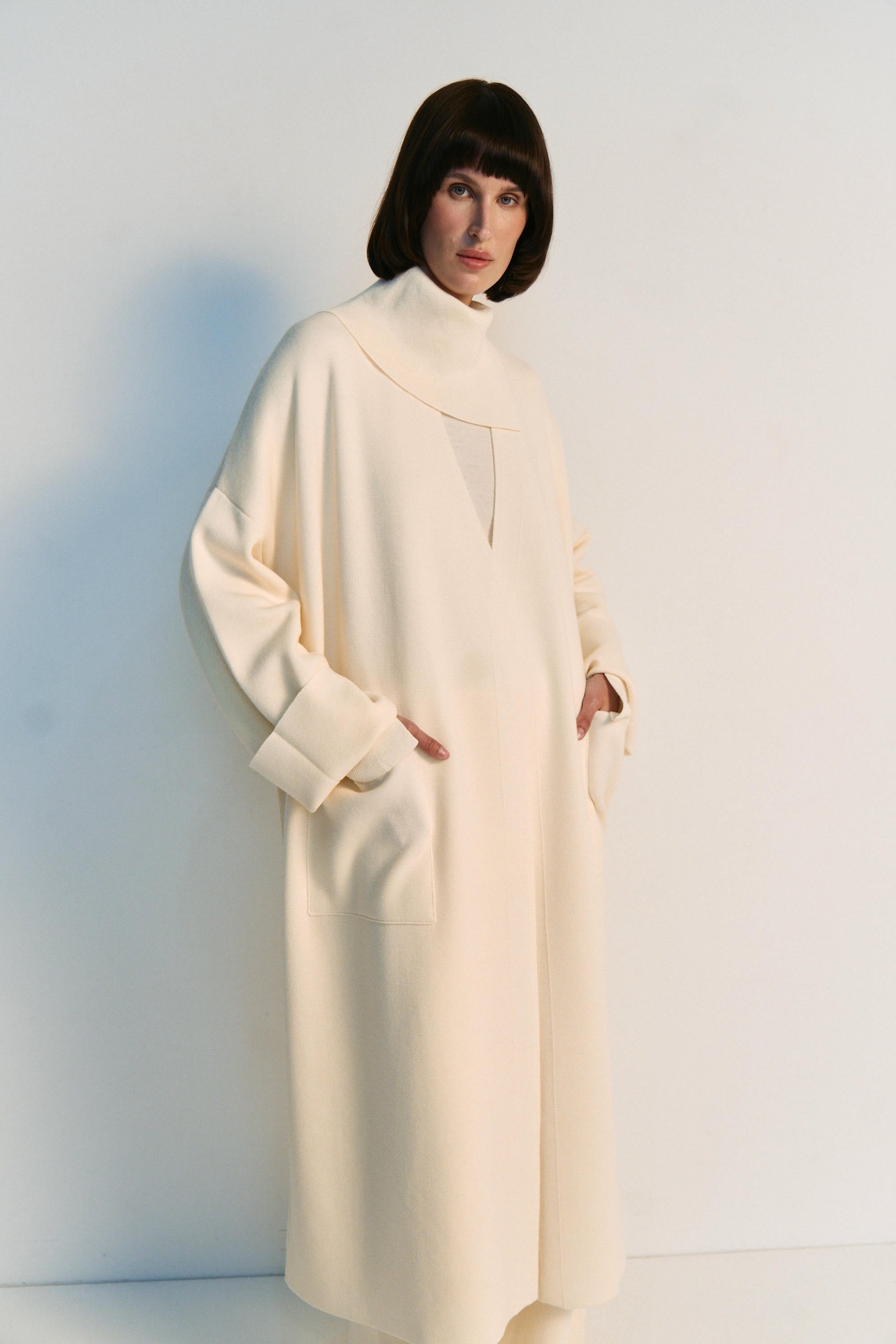 Person wearing a long white coat against a light background