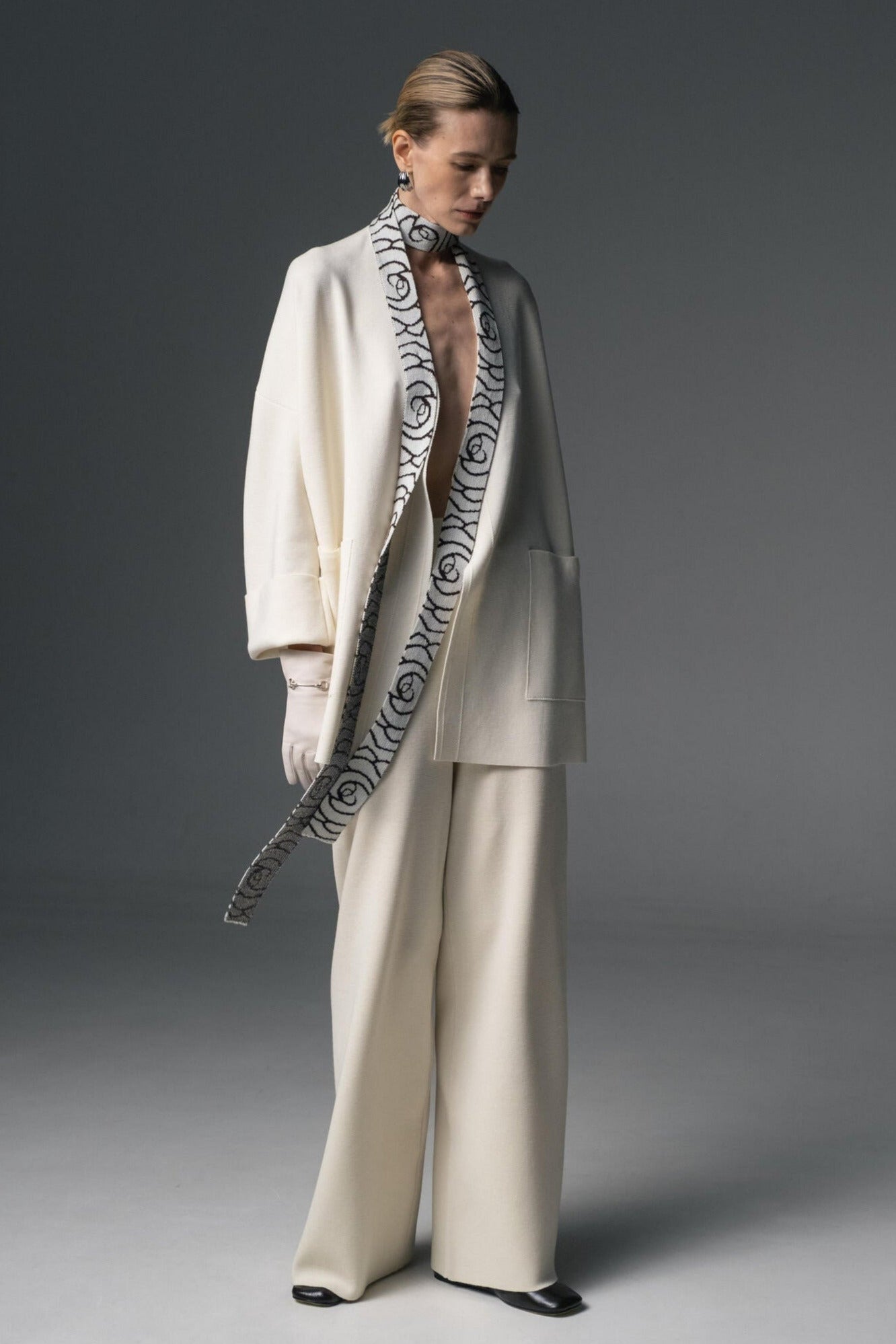 Person wearing a cream suit with a patterned scarf against a dark background.